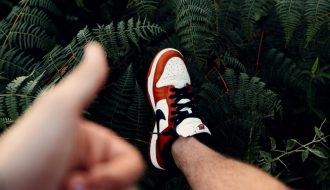 person in black white and orange nike sneakers standing on green fern plant
