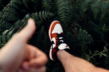 person in black white and orange nike sneakers standing on green fern plant