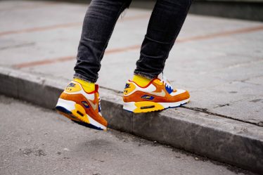 person wearing pair of orange-and-white Nike Air Max low-top shoes