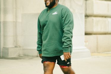 man in green sweater and black shorts running on road during daytime
