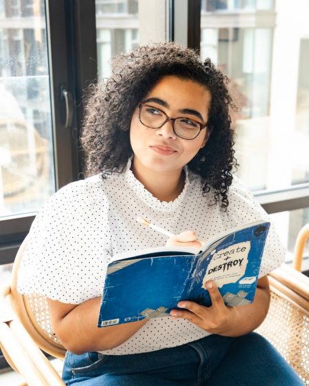 woman in white and black polka dot shirt holding blue and white book