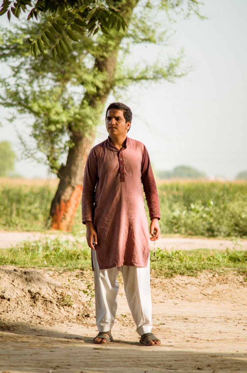 man in red long sleeve shirt and white pants standing on brown field during daytime