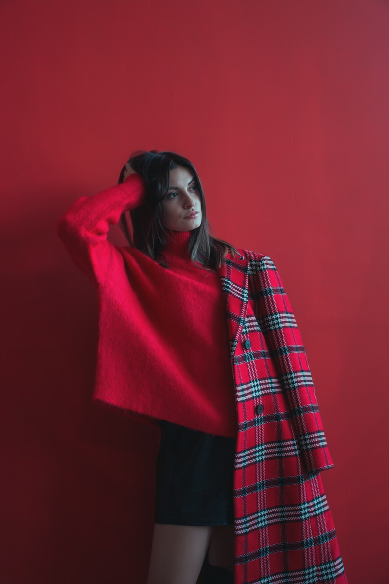 woman holding her head wearing red long-sleeved shirt and half of coat