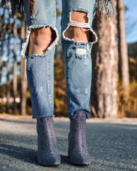 woman wearing distressed blue denim jeans and pair of purple glitter booties