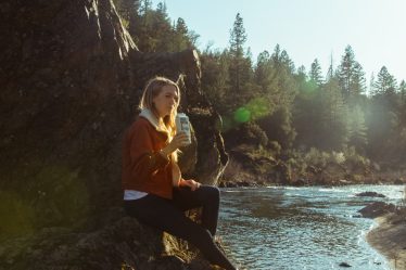 woman in blue long sleeve shirt sitting on rock near river during daytime