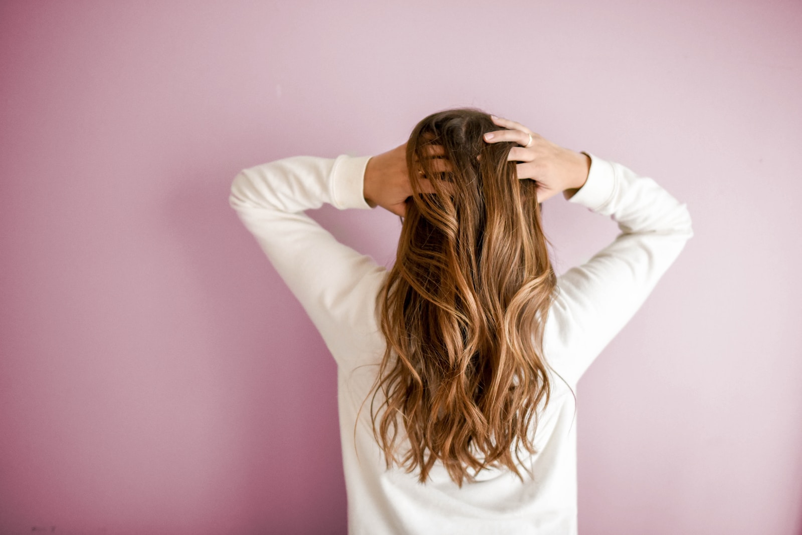 woman in white long-sleeved shirt standing in front of pink wall