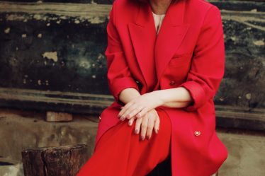 woman in red blazer and black skirt sitting on brown concrete stairs