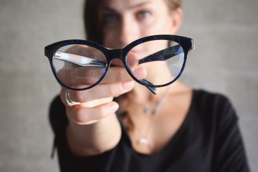 selective focus photo of eyeglasses hold by woman