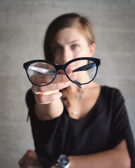 selective focus photo of eyeglasses hold by woman